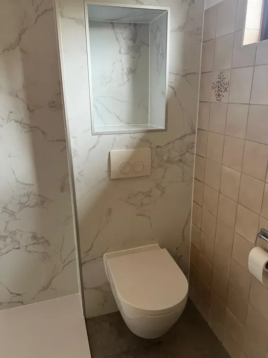 Hangtoilet tegen een marmerlook wand, met een nis boven de drukplaat
