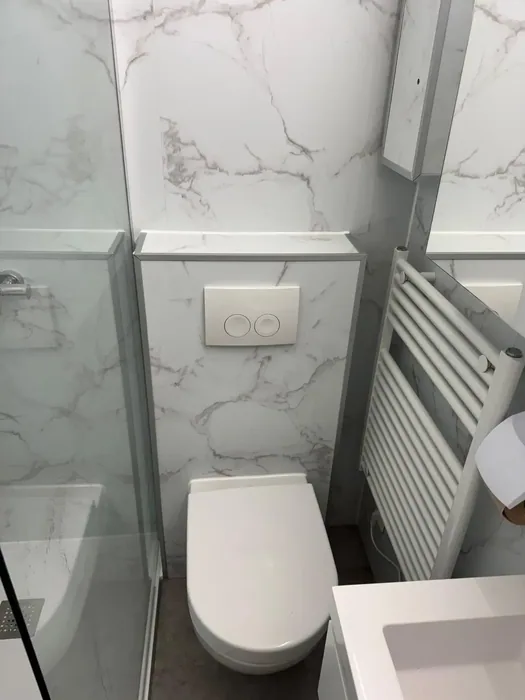 Wit hangtoilet op een voorzetwand met witte marmerlook panelen en een handdoekradiator