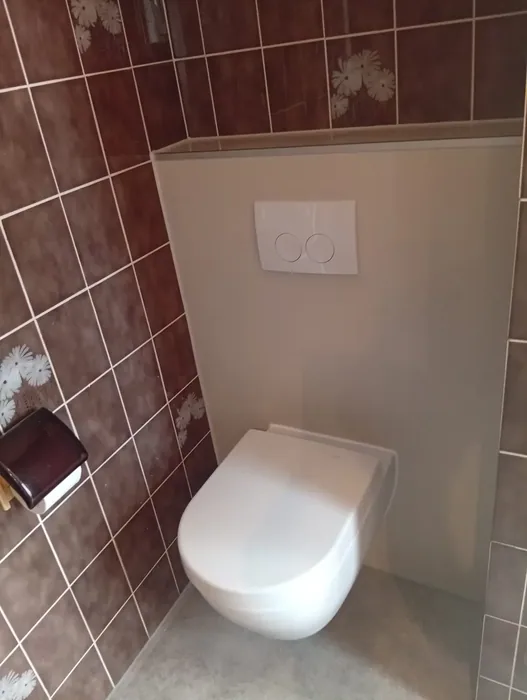 Dezelfde hoek na de renovatie: hangtoilet op een nieuwe witte voorzetwand tussen de bestaande bruine tegels