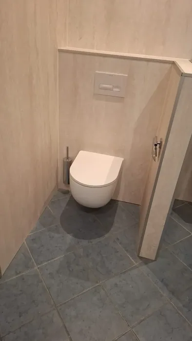 Hangtoilet tegen een voorzetwand met beige steenlook panelen en blauwgrijze vloertegels