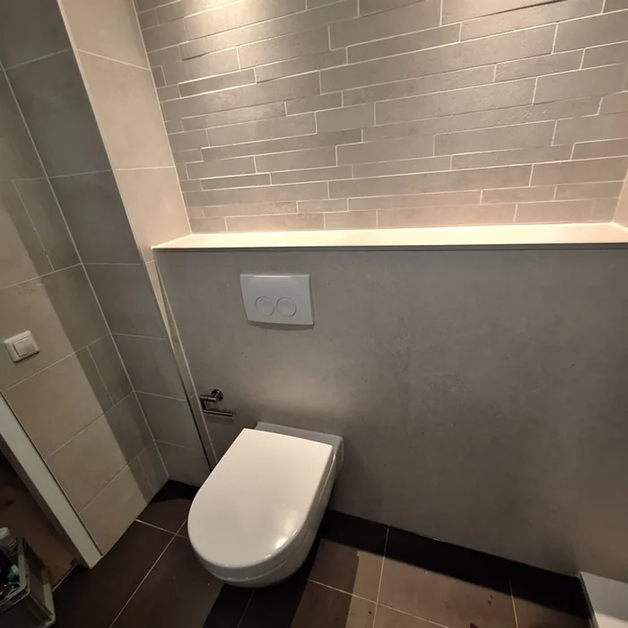 Hangtoilet onder een verlichte nis met een wand van smalle grijze stroken