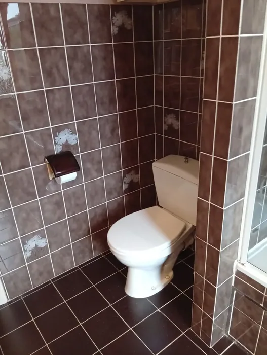 Oud staand toilet met opbouwreservoir tussen bruine wandtegels, vóór de renovatie