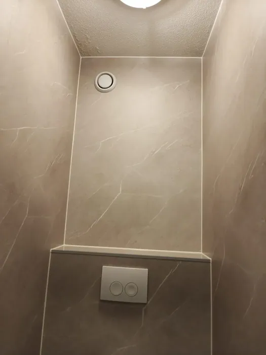 Toiletruimte met beige marmerlook panelen, voorzetwand met drukplaat en ventilatierooster in het plafond