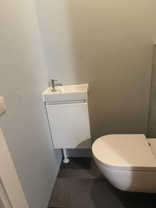 Wit fonteinmeubeltje naast een wit hangtoilet op een donkere vloer