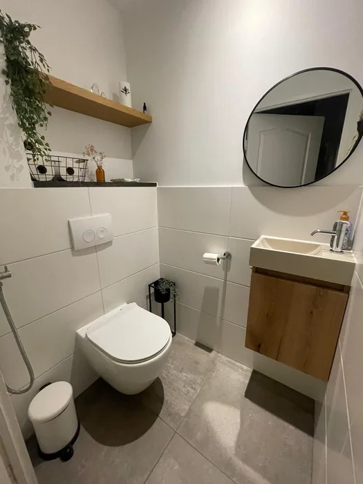 Toilet met hangtoilet, houten fonteinkastje, ronde zwarte spiegel en grote grijze vloertegels