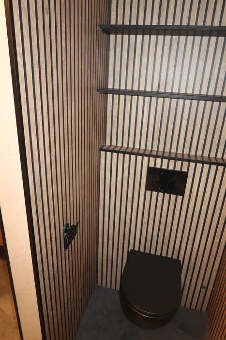 Drie zwarte wandplanken boven een zwart hangtoilet tegen een lamellenwand