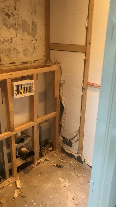 Toiletruimte na het slopen: houten regelwerk, inbouwreservoir en afvoer zichtbaar