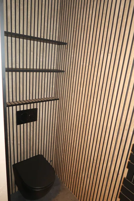 Toiletruimte met houten lamellenwand en zwart hangtoilet, gezien vanaf de deur