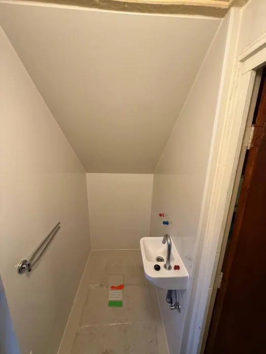 Smalle toiletruimte onder de trap met nieuwe witte wanden, fonteintje en steunbeugel, toilet nog niet geplaatst