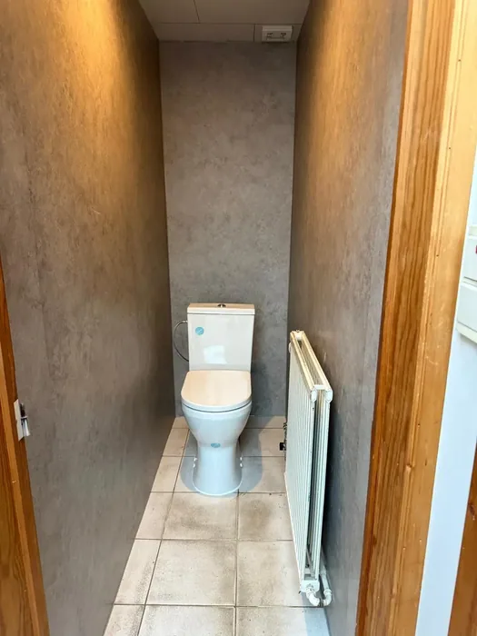 Smalle toiletruimte met betonlook wandpanelen, staand toilet en radiator