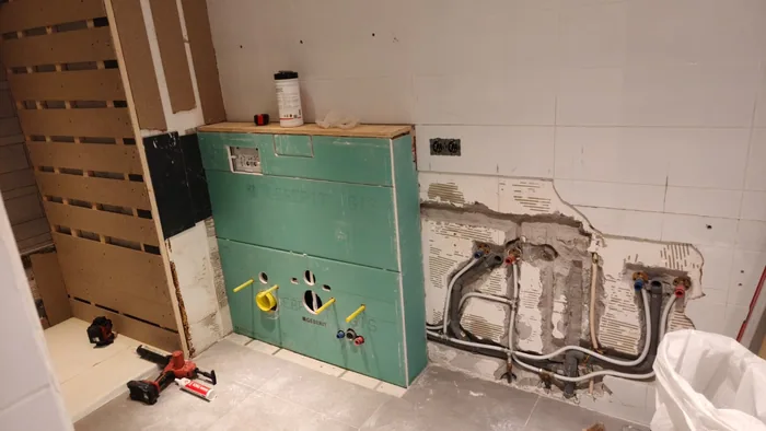 Voorzetwand in aanbouw met uitsparingen voor toilet en bidet, de oude leidingen ernaast