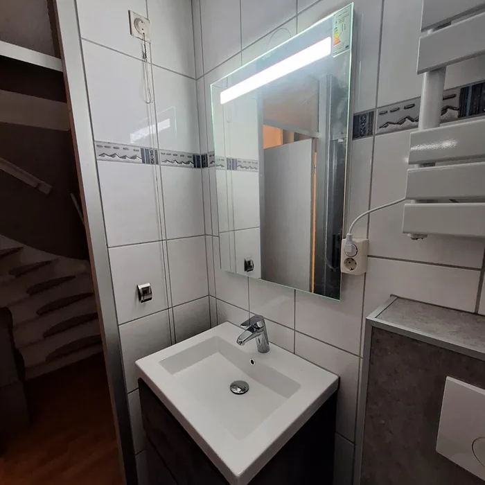 Wastafelmeubel met verlichte spiegel en handdoekradiator naast een trap, in hetzelfde huis als het kleine toilet