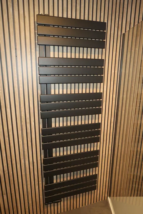 Zwarte designradiator op een houten lamellenwand in de badkamer van dezelfde woning